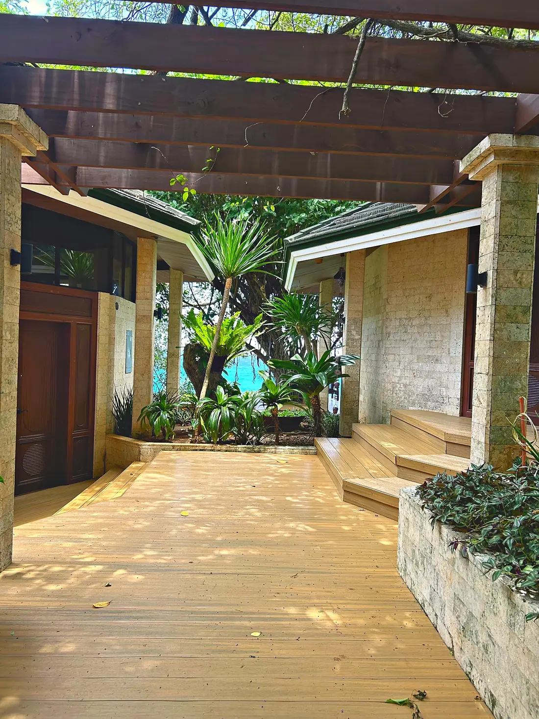Stone courtyard under a timber pergola, with a glimpse of the sea